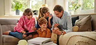 Eine Familie sitzt auf dem Sofa und bedient ein Handy und Tablet