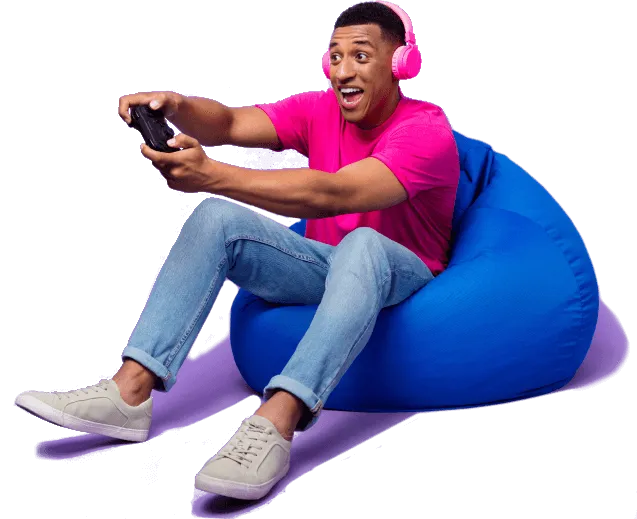 Junger man sitzt euphorisch im Sitzsack mit einem Gaming-Controller in der Hand und Kopfhörern auf den Ohren.